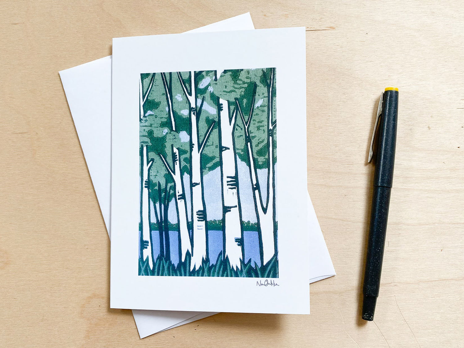 A single greeting card with an image of birch trees in the foreground and a lake in the background.