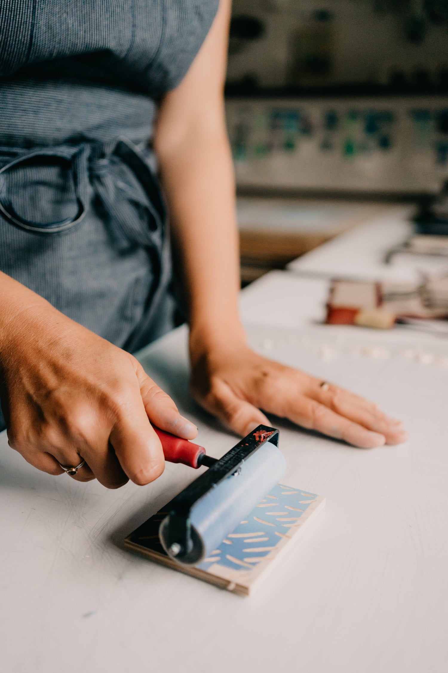 Nan Onkka's hands are shown rolling out ink onto a carved wooden block. She is working in her studio.